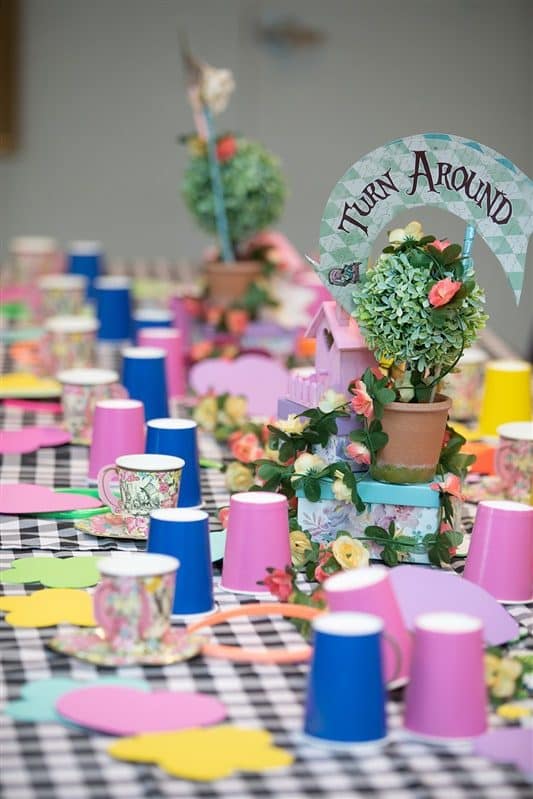 An Alice in Wonderland themed party table with colorful cups and topiaries