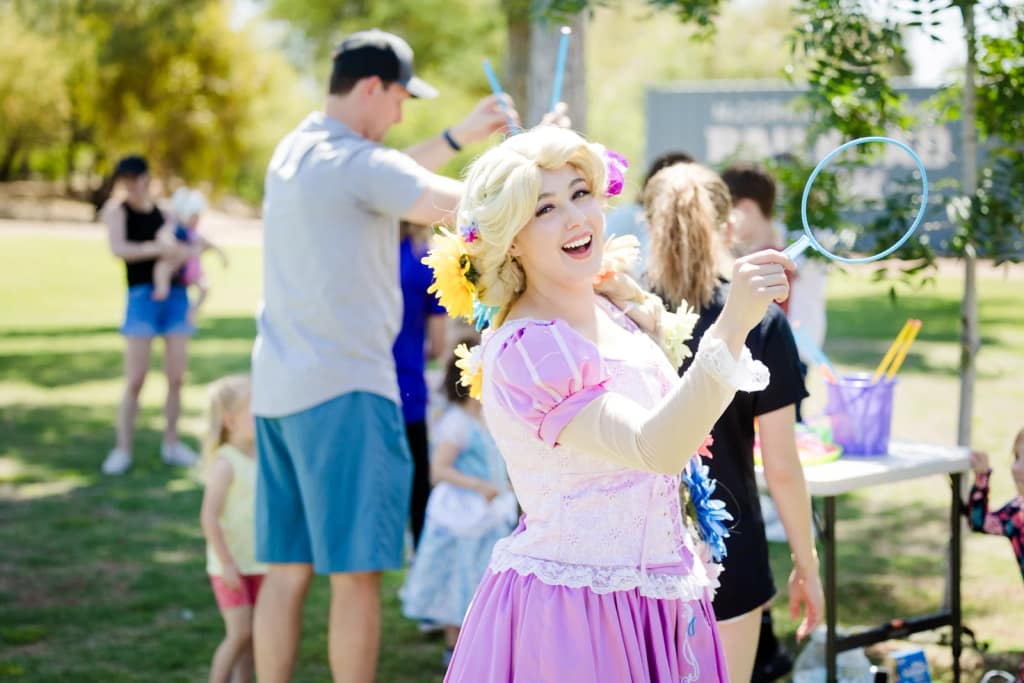 A Rapunzel character with a giant bubble wand delights guests at an outdoor party