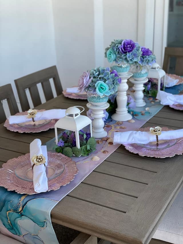 A mermaid-themed table setting with purple and teal floral centerpieces